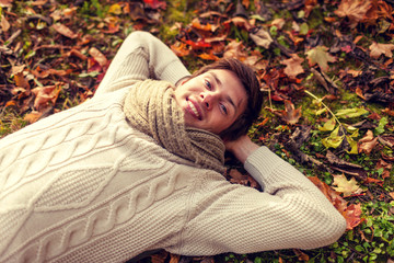 close up of smiling young man lying in autumn park