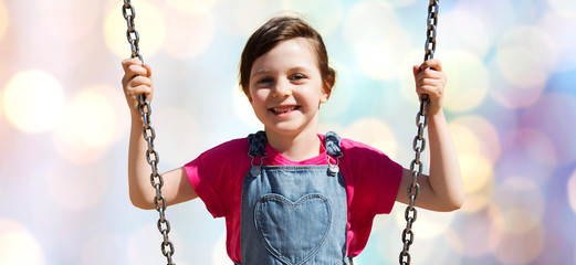 happy little girl swinging on swing over lights