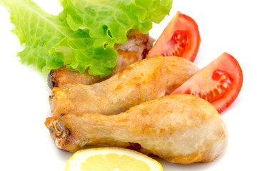 chicken legs on a white plate with slices of tomato and lettuce isolated on white background