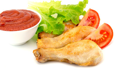 chicken legs dipped in ketchup on a white plate with lettuce and roasted potatoes isolated on white background