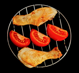 chicken legs on the grill with sliced tomato top view isolated on black background