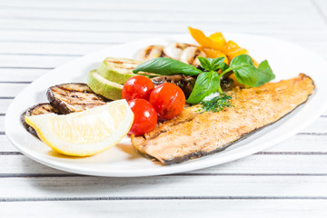 Tasty baked fish with grilled vegetables on  plate on wooden table close-up
