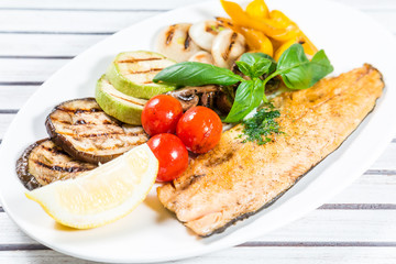 Tasty baked fish with grilled vegetables on  plate on wooden table close-up