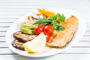 Tasty baked fish with grilled vegetables on  plate on wooden table close-up