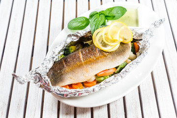 Tasty baked fish with grilled vegetables on  plate on wooden table close-up