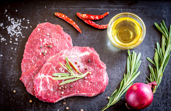 Fresh beef steaks with ingredients on the dark background