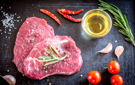 Fresh beef steaks with ingredients on the dark background