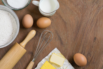 Baking cake in rural kitchen - dough recipe ingredients (eggs, flour, milk, butter, sugar) and rolling pin on vintage wood table from above. Rustic background with free text space.