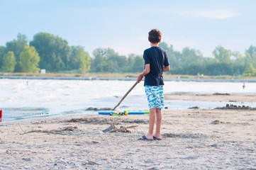 boy palying with a stick on a sandy beach in summer