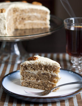 Slice of hummingbird cake with whole cake and coffee in background