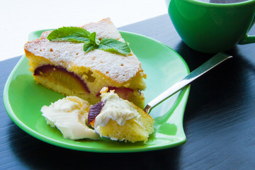 Piece of plum cake with cream on a green plate near the cup of tea