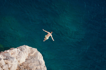 Young man jumping from cliff into sea. - Powered by Adobe