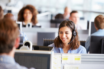 Young woman working in call centre, surrounded by colleagues - obrazy, fototapety, plakaty