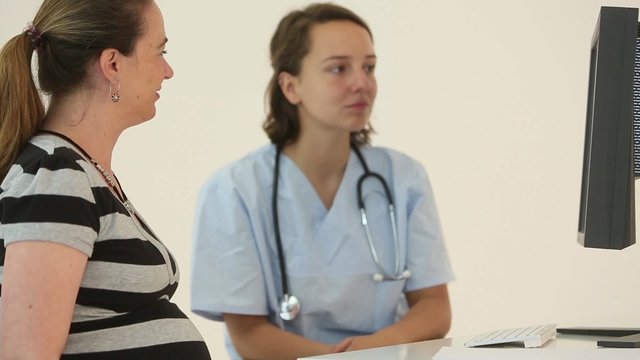 Young and cute female doctor talking to her pregnant patient looking at baby results on computer