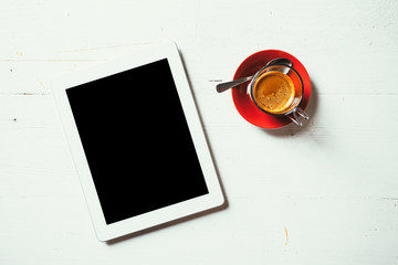 On a wooden table painted white are placed two objects: a digital tablet and coffee espesso. Top view