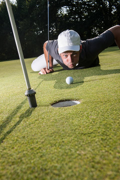 Golfer lying down on the green, blowing on his ball