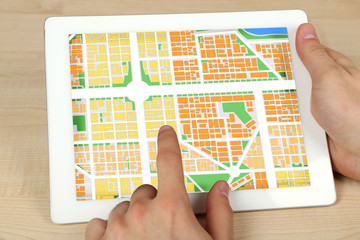 Male hands holding tablet pc with map gps navigation application on wooden table