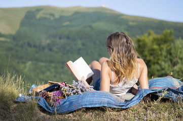 Girl laying on a blanket and reading a book on a picnic in the f