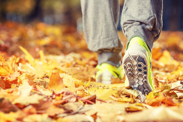 Runner woman feet running on autumn road closeup on shoe. Female fitness model outdoors fall jog...