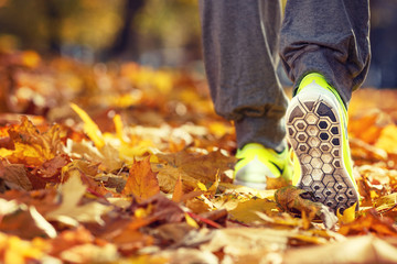 Runner woman feet running on autumn road closeup on shoe. Female fitness model outdoors fall jog...