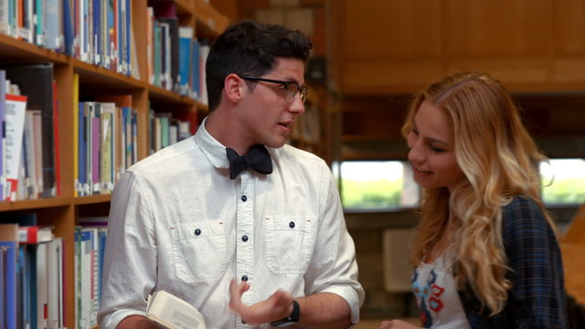 Pretty student talking to nerd in library