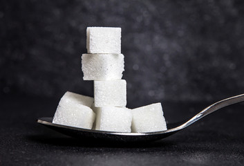cloose up white sugar cubes in metal spoon on black stone plate