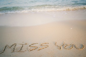 The word miss you written in sand on beach