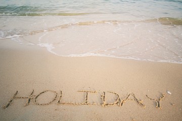 The word holiday written in sand on beach