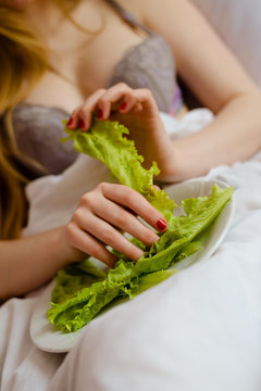 Girl in lingerie with perfect breasts taking leaf of lettuce