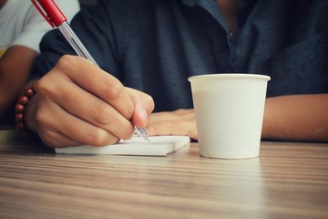 Woman with pen writing on paper and coffee cup