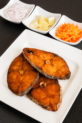Indian seer fish fillets fry - Closeup of delicious seer/mackerel fish fillets fry served with shredded carrots, raw onion rings, lemon. The fish is marinated in cayenne pepper, salt and deep fried.