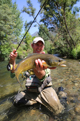 Fly fisherman holding brown trout in stream water © goodluz
