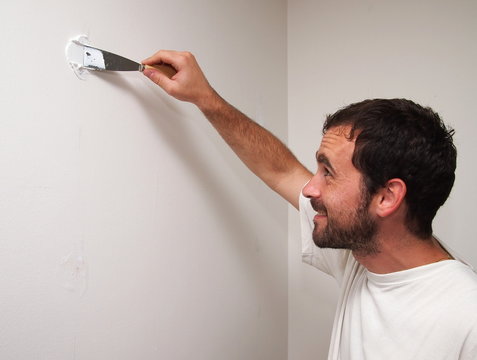 Black-haired man covering a hole in the white wall with a bricklayer cement (putty).
