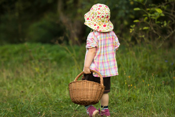 baby girl in sunhat standing on green grass with woven basket