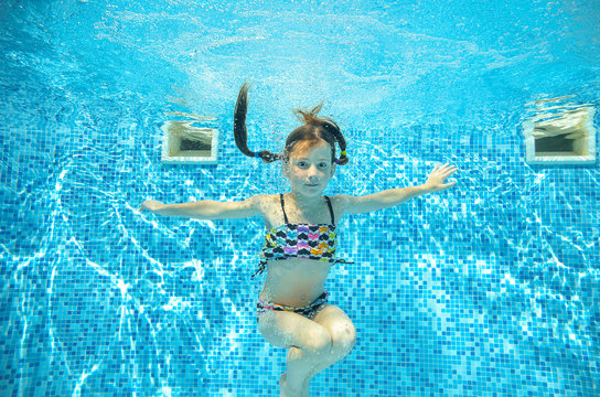Girl jumps and swims in pool underwater, happy active child has fun in water