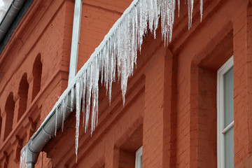 Grosse Eiszapfen haengen an der Dachrinne eines Backsteingebaeudes