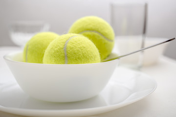 Tennis balls are in a bowl instead of ice cream, symbolizing changes and refusal of desserts and sweet and replacement of sports and healthy lifestyle. White variant.