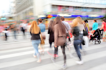 Motion blurred pedestrians crossing sunlit street. Intentional motion and panning blur.