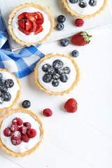 Dessert tartlets with berries on white wooden background