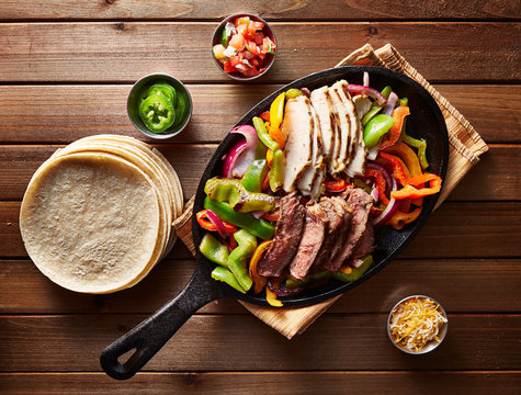 top down photo of mexican steak and chicken fajitas in iron skillet with corn tortillas