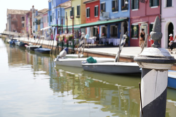 Fototapeta na wymiar In the foreground one pole painted with black and white stripes in the background (out of focus) the colorful houses and one canal of Burano Island, Venice, Italy.