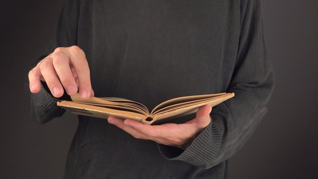 Adult man reading old vintage book with yellow pages, turning pages and looking at text, close up image with selective focus, 4k uhd footage