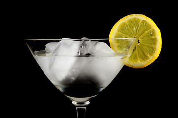 glass of drink with ice and lemon slice close-up isolated on a black background
