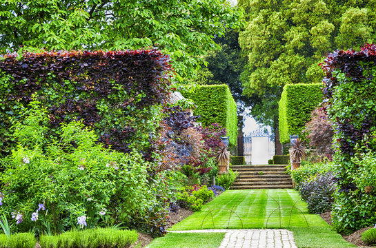 Formal summer garden with grass path to stone stairs and iron gate
