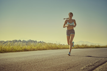 Active sporty woman in summer sportswear running, sprinting on a road at sunrise or sunset. Health care, body care, healthy lifestyle, willingness concept. Toned color edit.