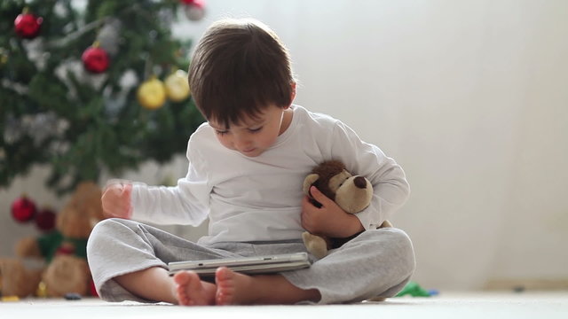 Cute little boy and his monkey toy, playing on tablet