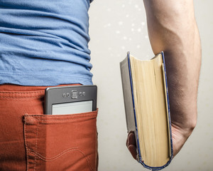 in the back pocket of jeans is an e-book, and in the man's hand a thick old paper book