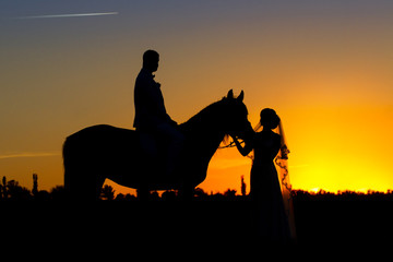 Couple in wedding day with horse silhouette against sunset sky