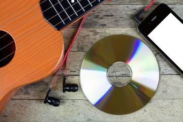 Guitar, CD disc, smart phone and earphones on a table