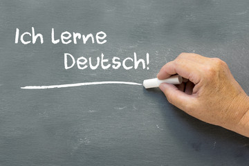 Hand on a chalkboard with the German words Ich lerne Deutsch (I